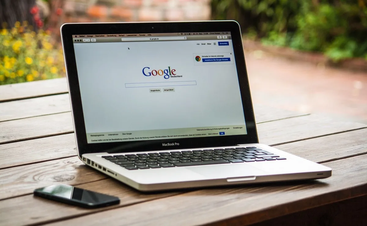 MacBook exibindo a busca do Google sobre uma mesa de madeira