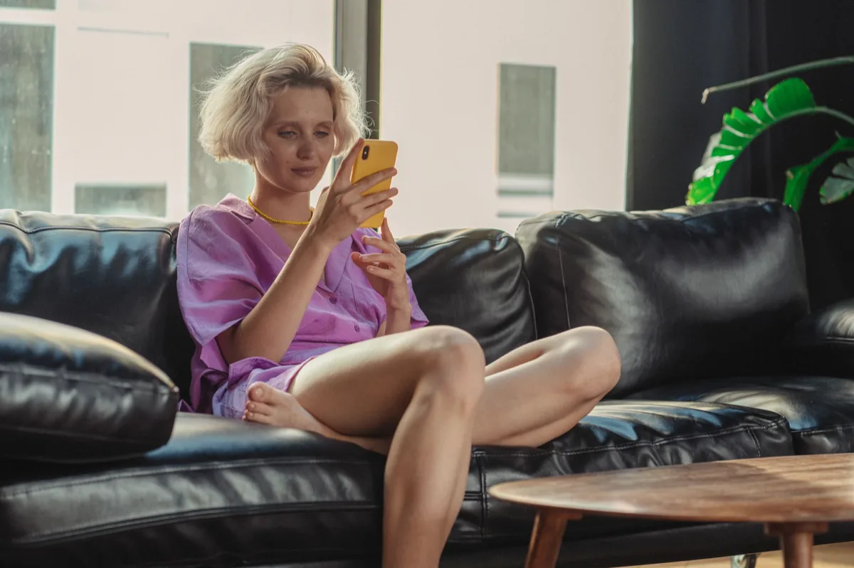 Mulher usando smartphone sentada em sofá com luz natural